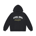 Front view of the Akali Essentials™ black heavyweight oversized hoodie featuring white collegiate text reading STEEL SOUL layered over gold cursive script.