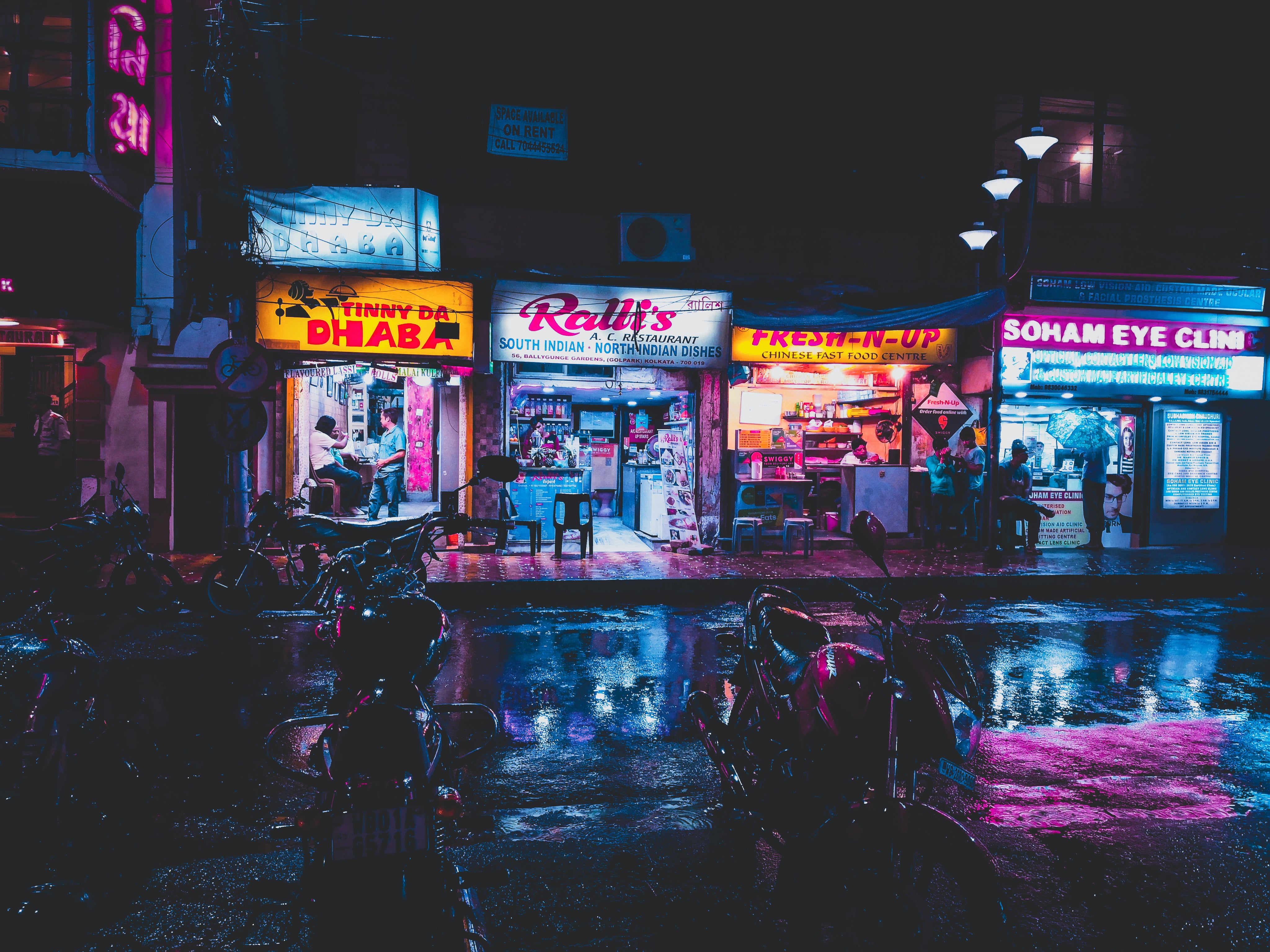 Up The Ante media layout showing a vibrant neon-lit South Asian street food night market scene with parked motorcycles.